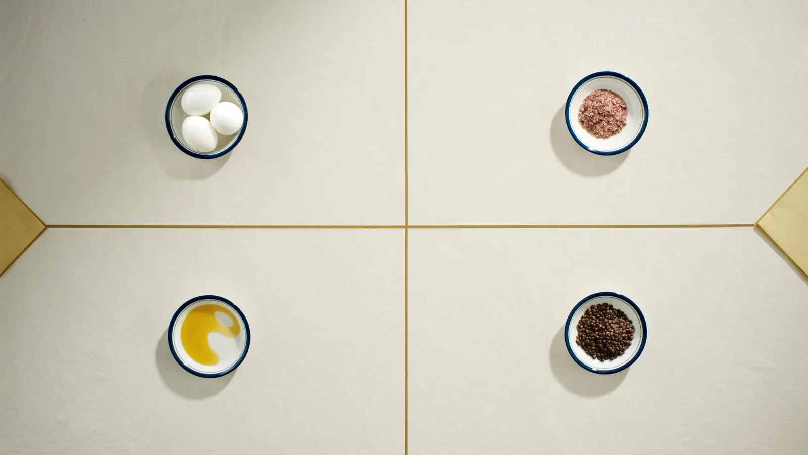 Editorial overhead of four small porcelain dishes on cream linen — eggs, oats, olive oil, lentils — with hairline gold dividers.