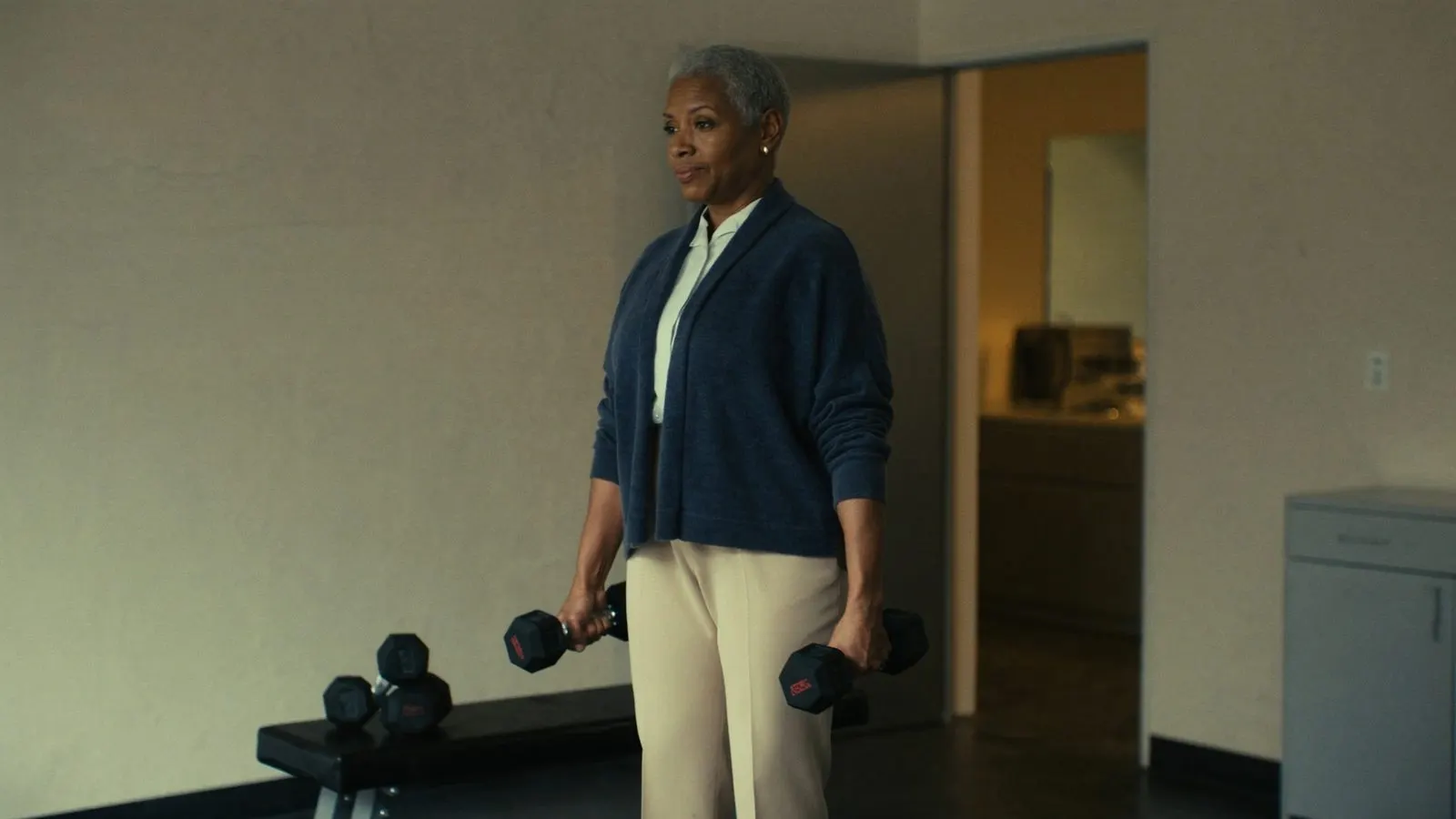 Editorial portrait of a 50-year-old woman mid-deadlift in a minimalist training studio, navy and cream wardrobe.