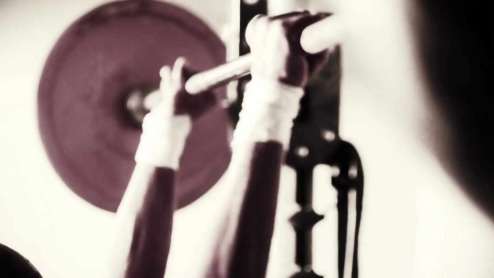 Editorial close-up of mature hands gripping a barbell at a power rack, cream linen wraps visible, soft daylight.