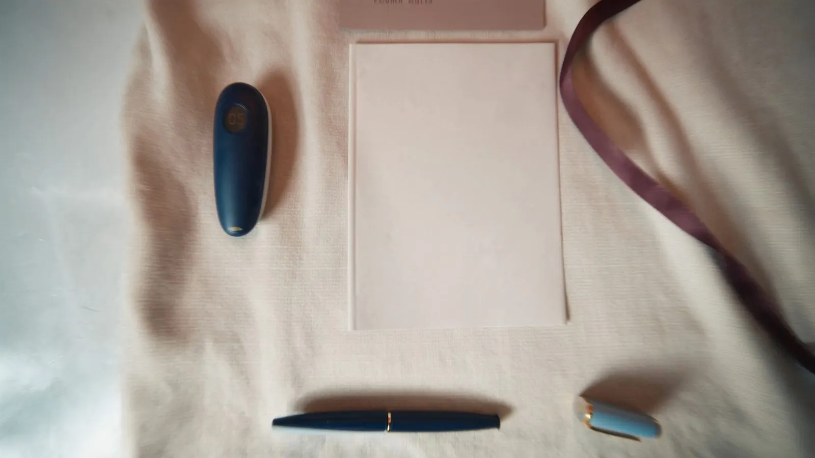 Editorial close-up of a continuous glucose monitor on cream linen with a dusty rose silk ribbon.