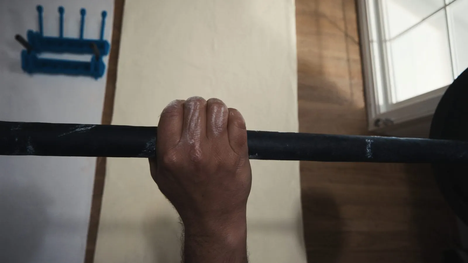 Editorial close-up of a single hand gripping a bar with chalk visible on cream linen background, soft daylight.