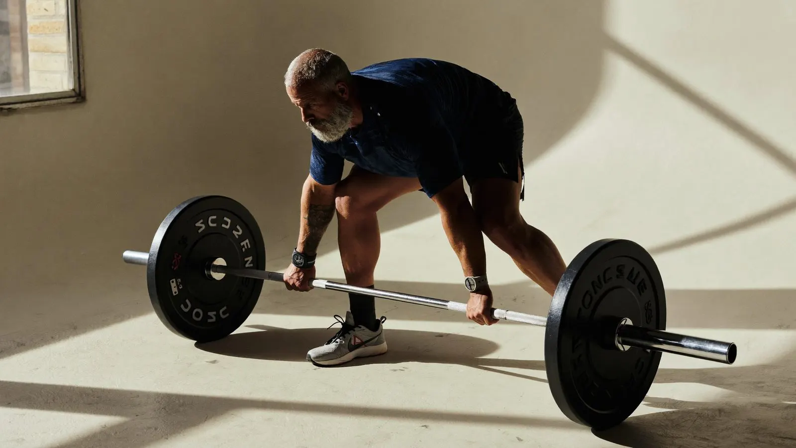 Editorial close-up of a person in their fifties performing a kettlebell deadlift in a sunlit studio