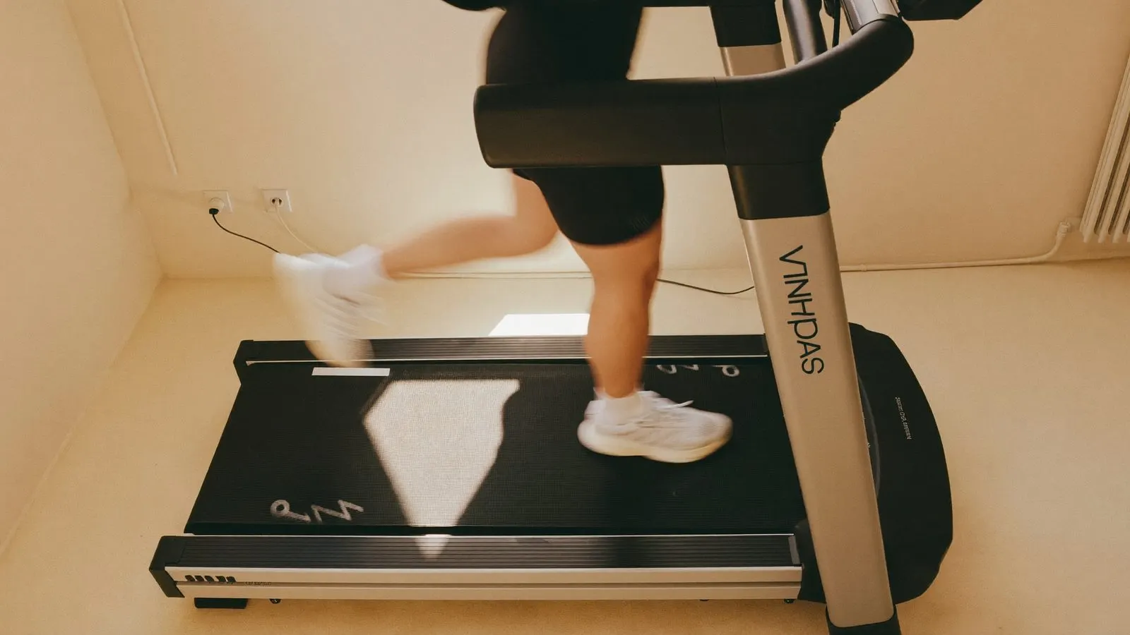 Editorial overhead view of a person mid-stride on a treadmill in a sunlit clinical studio space