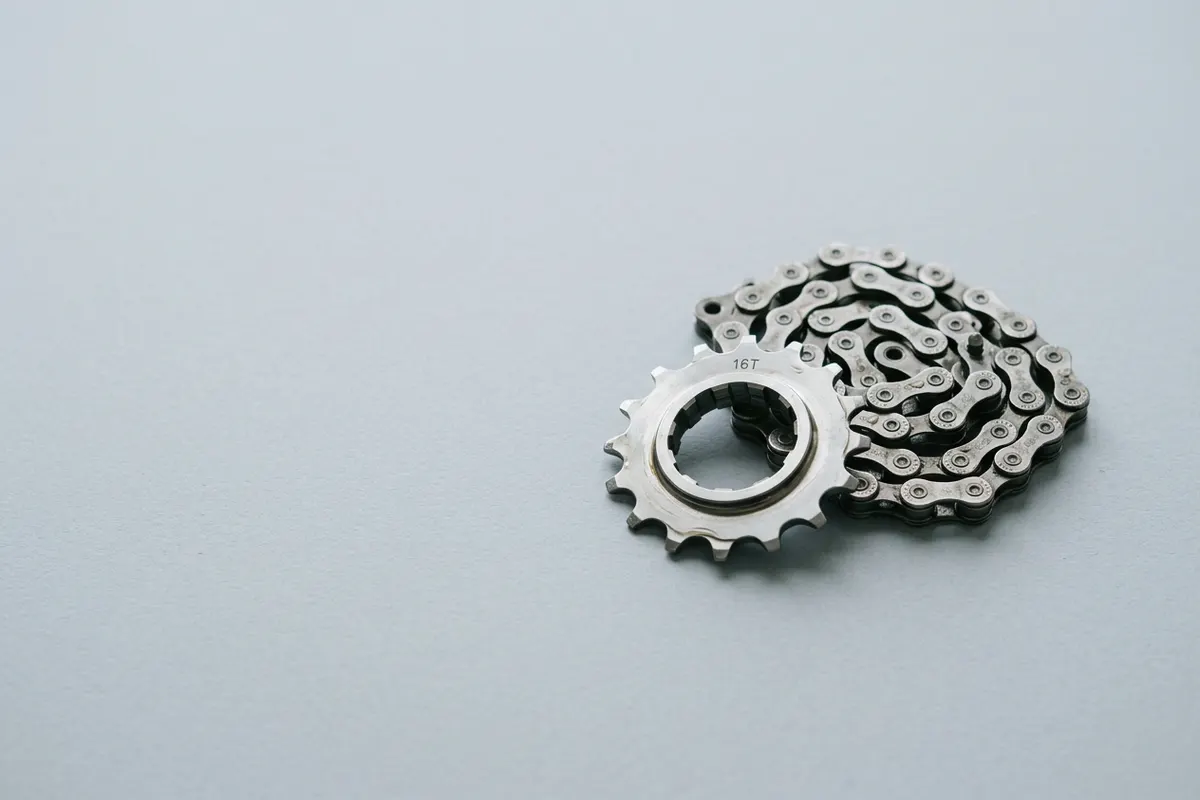 A coiled bicycle chain beside a steel sprocket