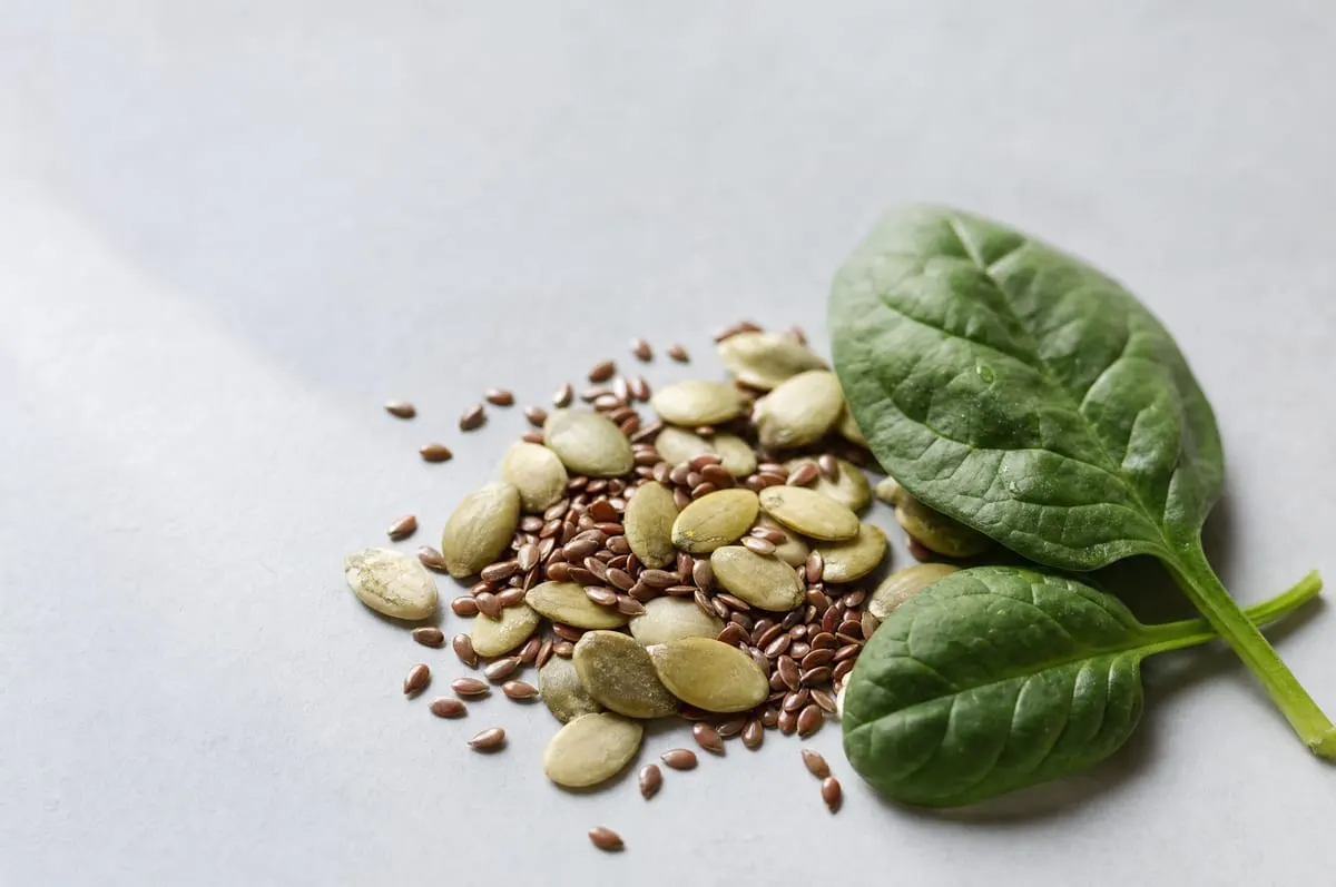 Pumpkin and flax seeds beside fresh spinach leaves
